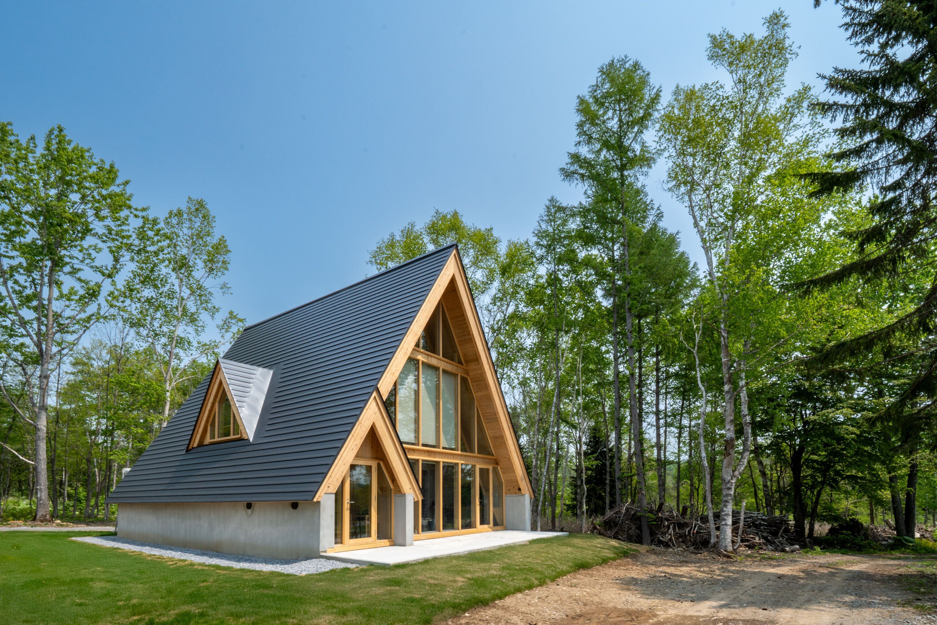 A modern, A-frame wooden house with large windows, surrounded by a forest.