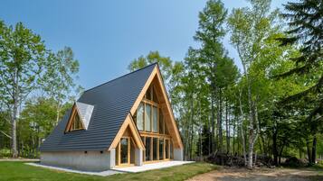 A modern, A-frame wooden house with large windows, surrounded by a forest.
