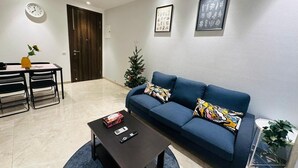En moderne stue med en mørkeblå sofa, et sofabord, et lille fjernsyn og et ur på væggen.