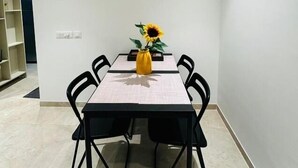 A dining area with a table, chairs, a clock, and a wall-mounted electrical panel. - 1BR Service Apartment A - 1008 Powai By Florastays (Mumbai)