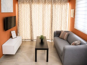 A modern living room with a grey sofa, a white side table, a black coffee table, and a patterned curtain. - Happiness and Love 5A – Central and Comfortable in Curaçao (Willemstad)