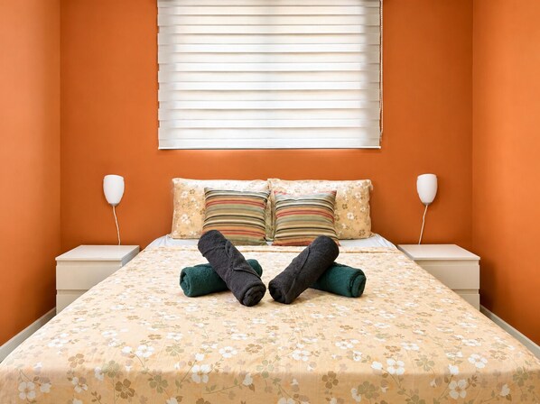 A bed with floral bedding, two pillows, and a pair of rolled-up dark green towels. - Happiness and Love 5A – Central and Comfortable in Curaçao (Willemstad)