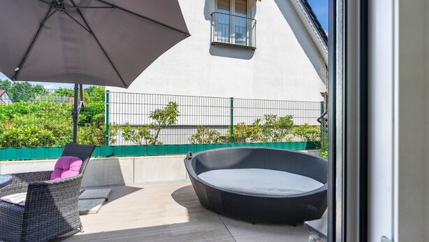 Une terrasse extérieure avec un fauteuil en osier, une jardinière ronde en osier et un grand parasol.