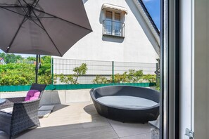 Eine Terrassengruppe mit Korbmöbeln, einem runden Becken aus Korbgeflecht und einem großen Sonnenschirm.