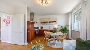 Une cuisine moderne avec des meubles en bois, un coin repas avec une table ronde et des chaises, et un salon avec un canapé et un coussin vert.