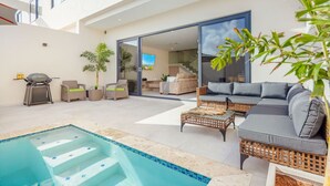 Un espacio exterior moderno con piscina, mobiliario y una parrilla.