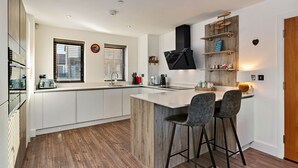 Et moderne køkken med en central ø, barstole, trægulv og integreret hårde hvidevarer.