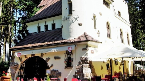 A building with a white facade and a stone base, featuring a large arched entrance and outdoor seating area with tables and chairs. - REZIDENCE ZÁMEČEK - BOUTIQUE HOTEL (Františkovy Lázně)