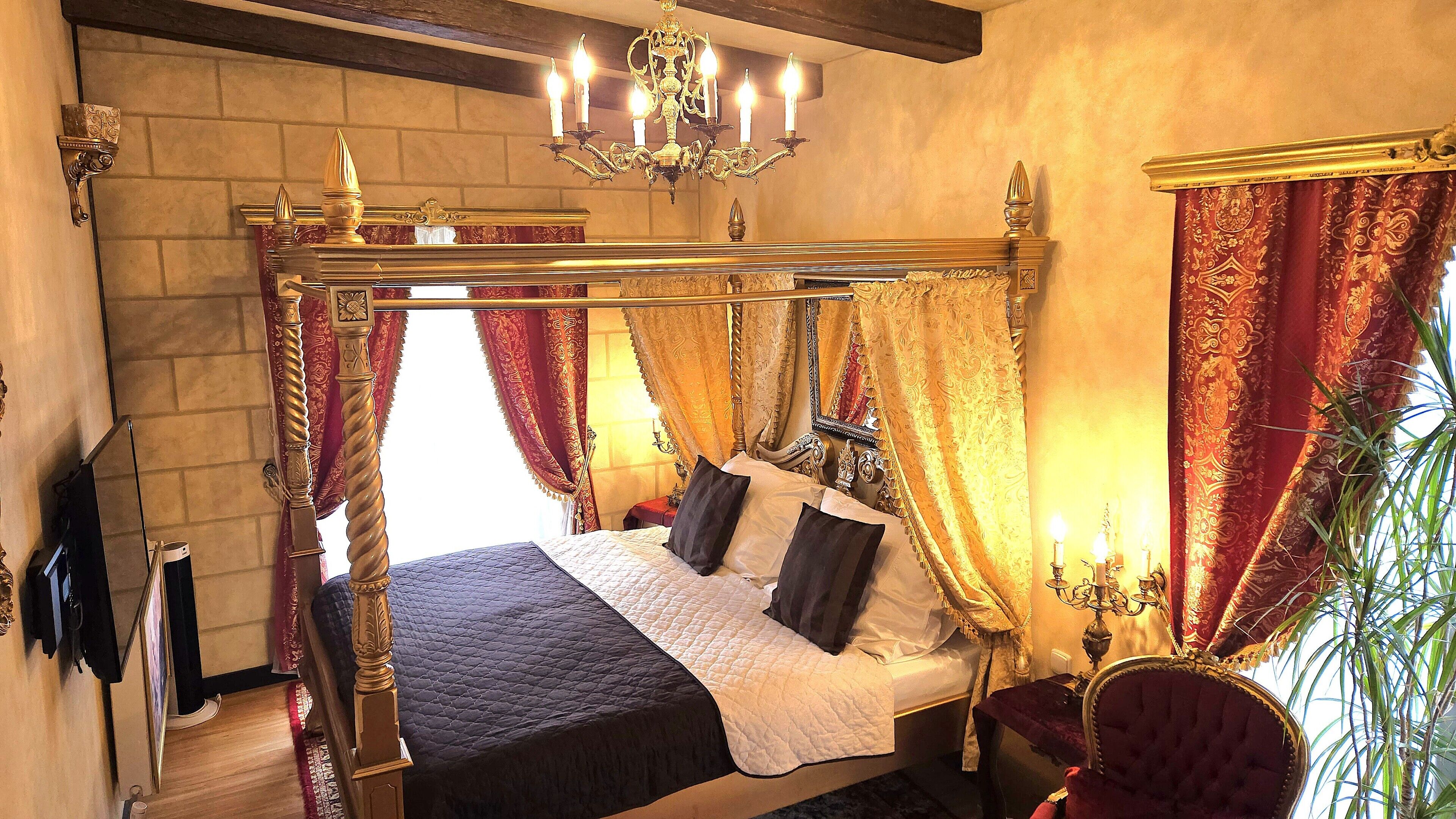 A four-poster bed with ornate curtains, a chandelier, and a mirror above the bed.