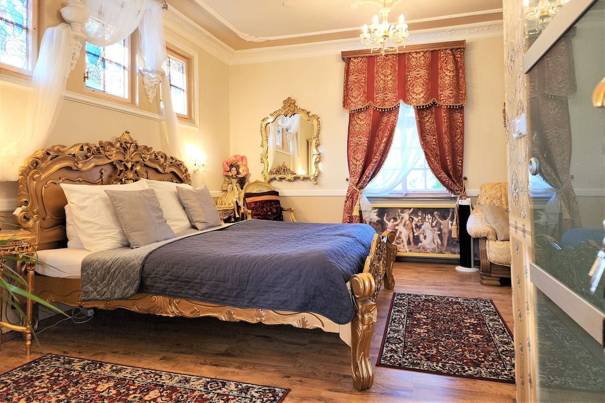 A bedroom with a large bed, ornate headboard, and a chandelier.