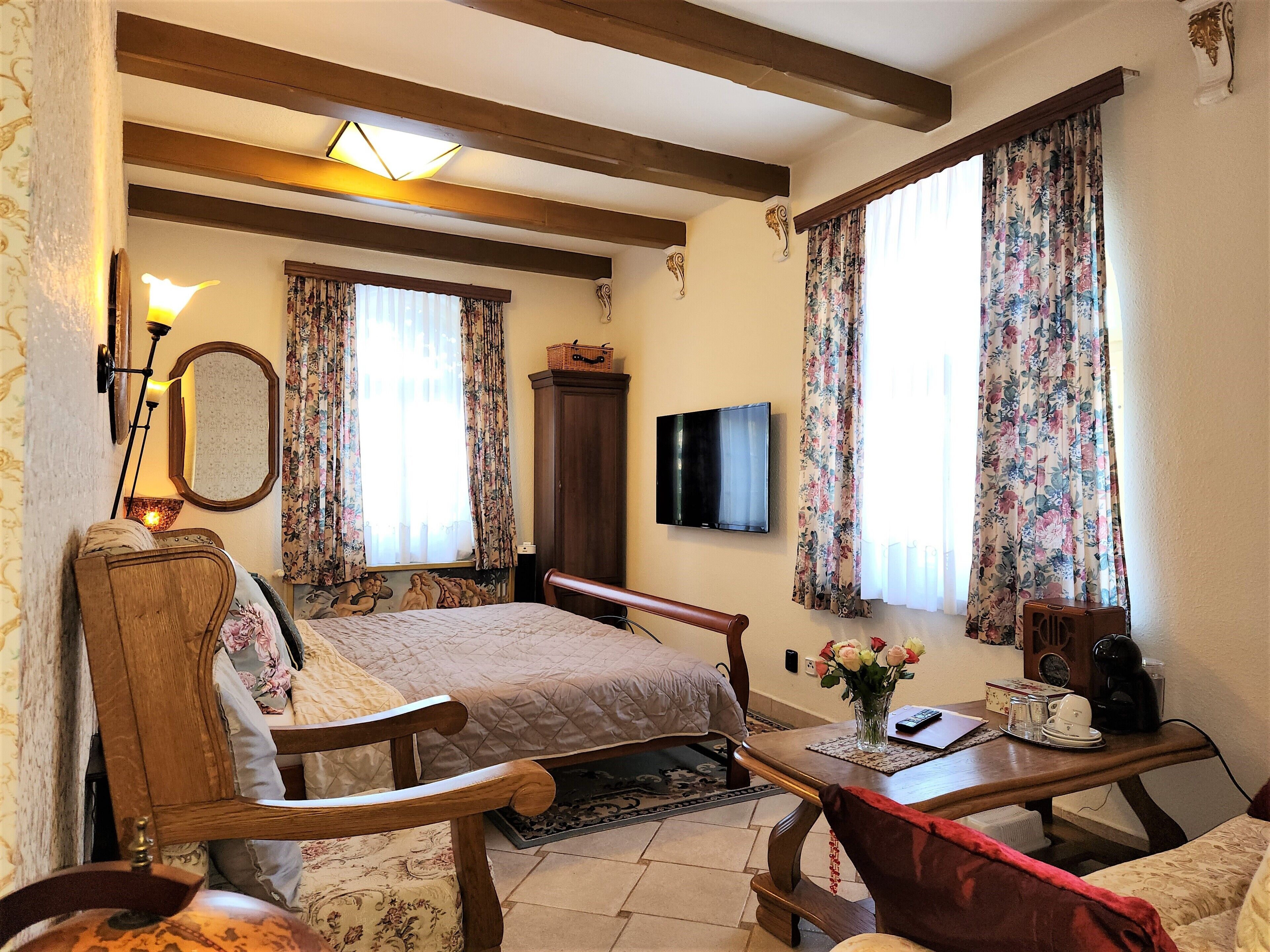 Een kamer met een bed, houten meubels, een televisie en gordijnen met bloemenprint.
