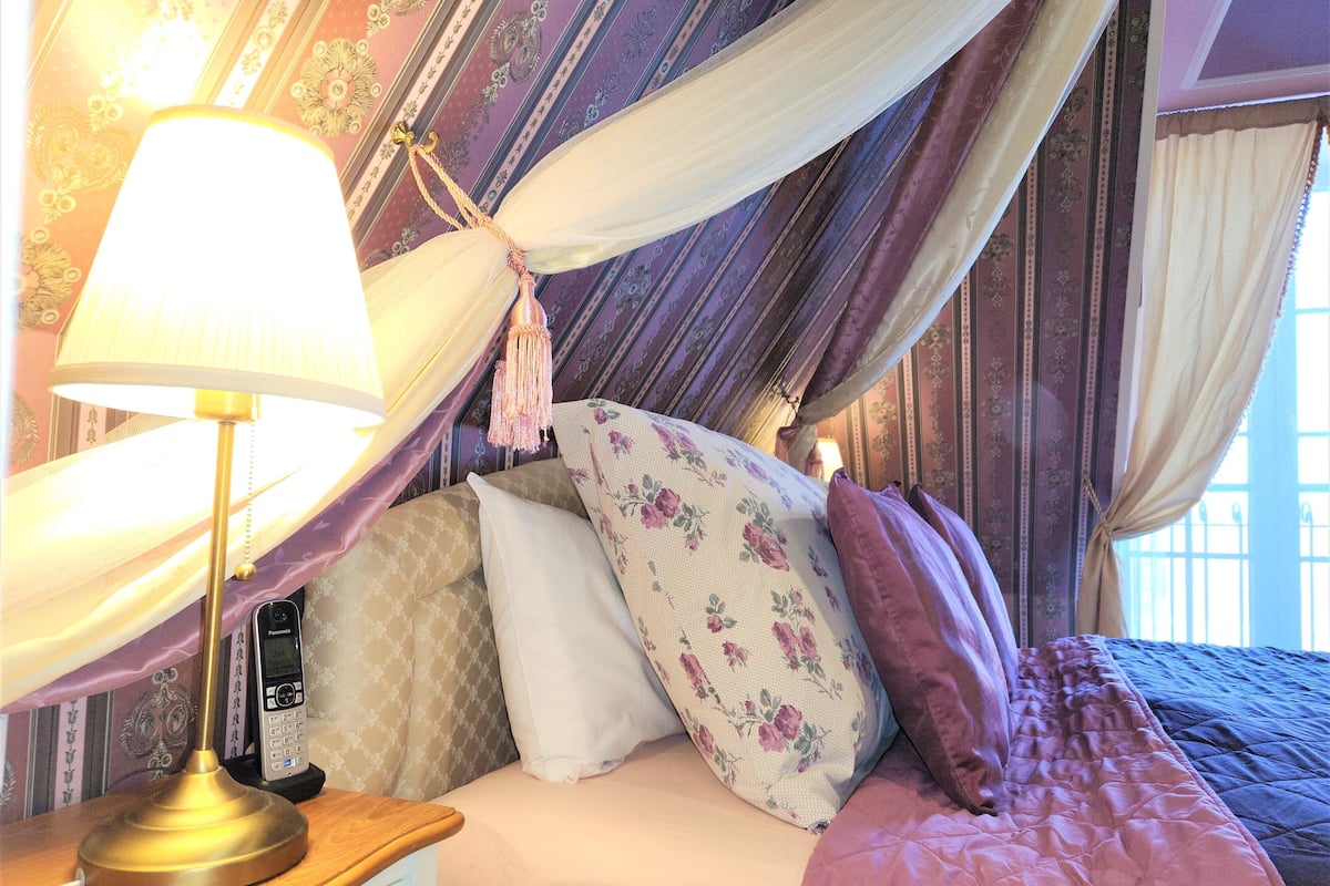 A bedroom with a canopy bed, a bedside lamp, and a telephone.