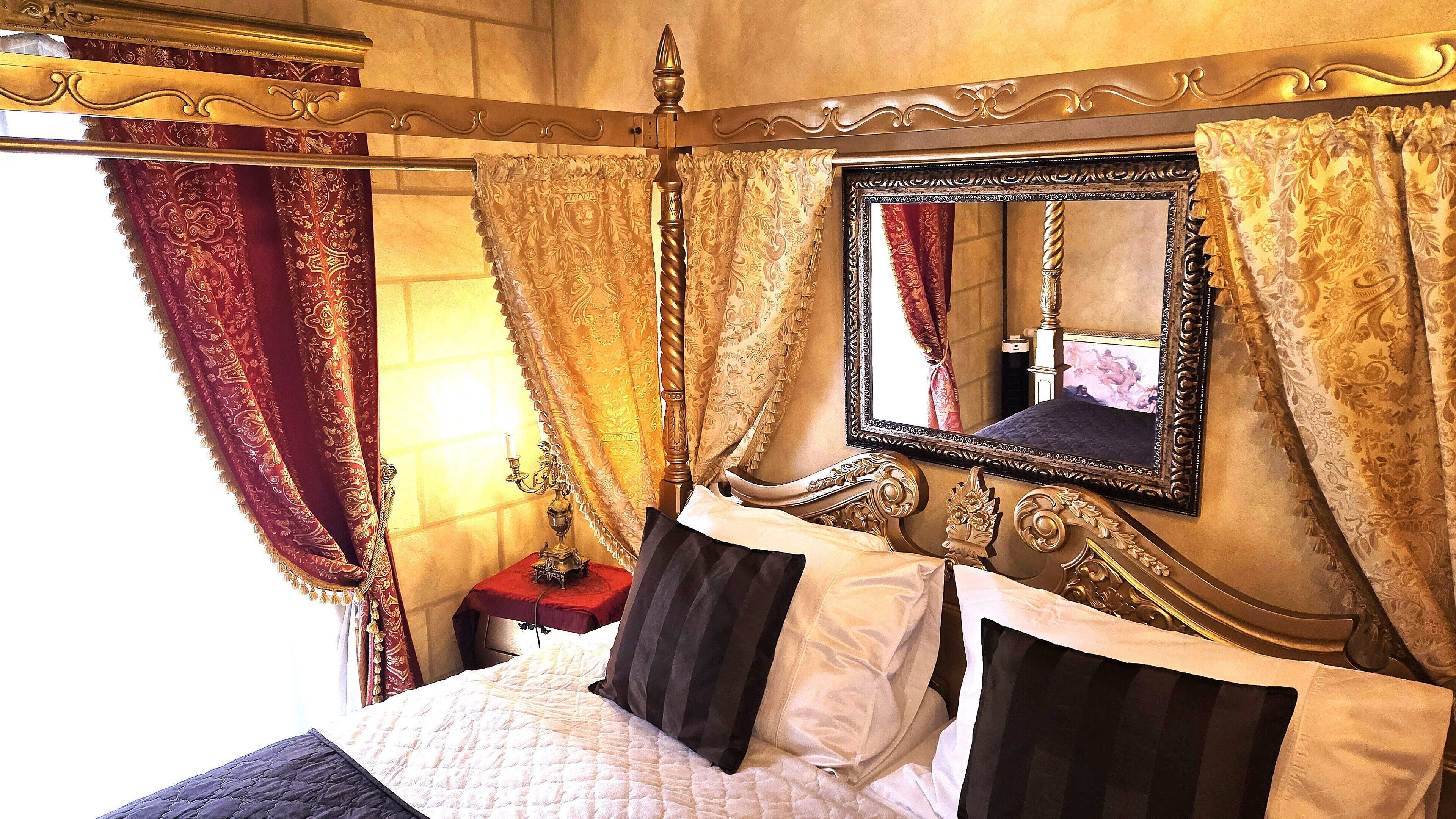 Un dormitorio lujoso con una cama con dosel, cortinas ornamentales y un espejo grande.
