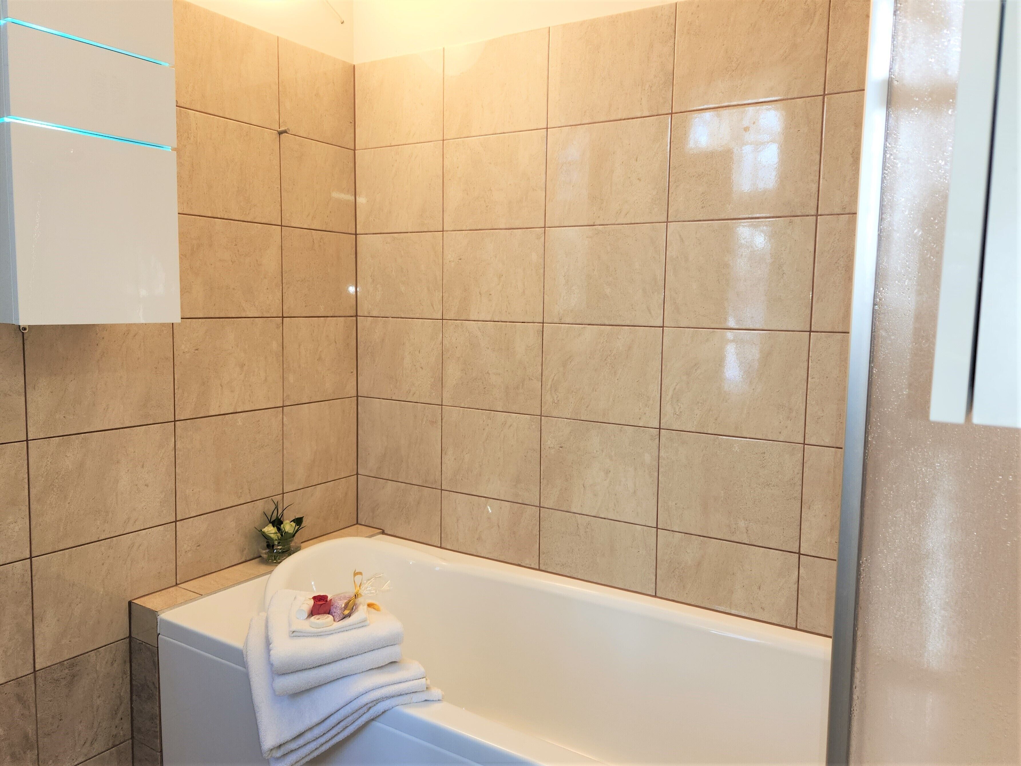 Un baño con bañera, azulejos color beige y un perchero con toallas.
