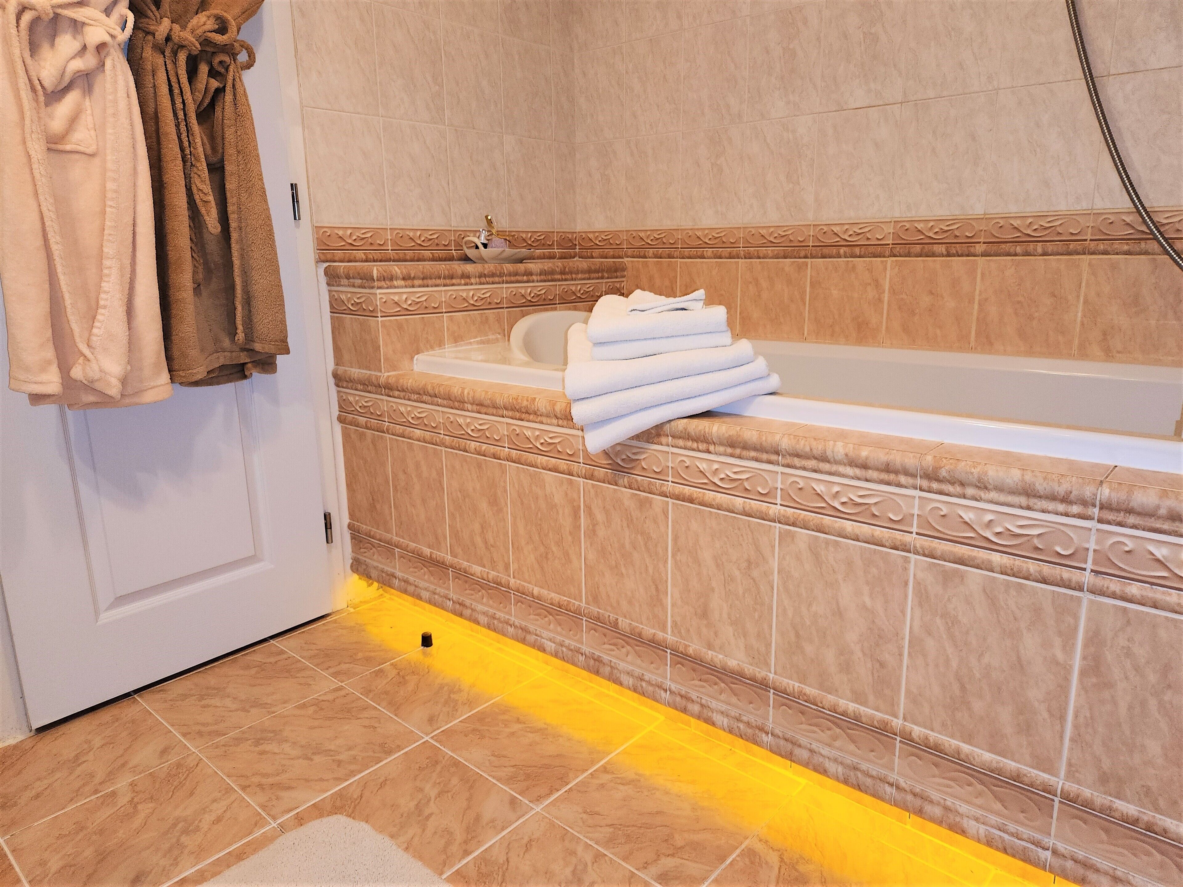 Un baño con bañera, un perchero con toallas y un borde decorativo de azulejos.