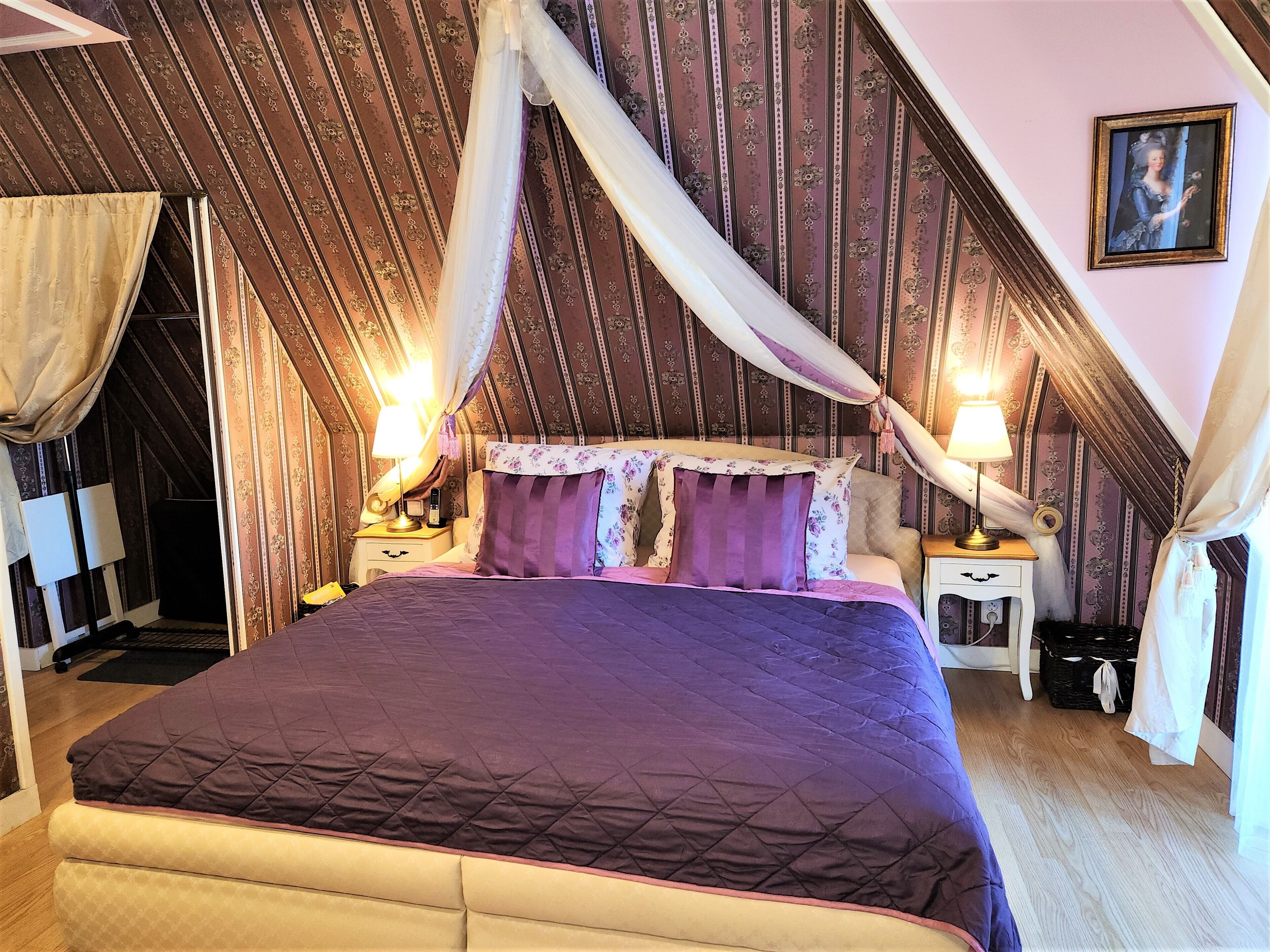 Une chambre à coucher avec un grand lit, deux tables de chevet, une petite table et un tableau accroché au mur.
