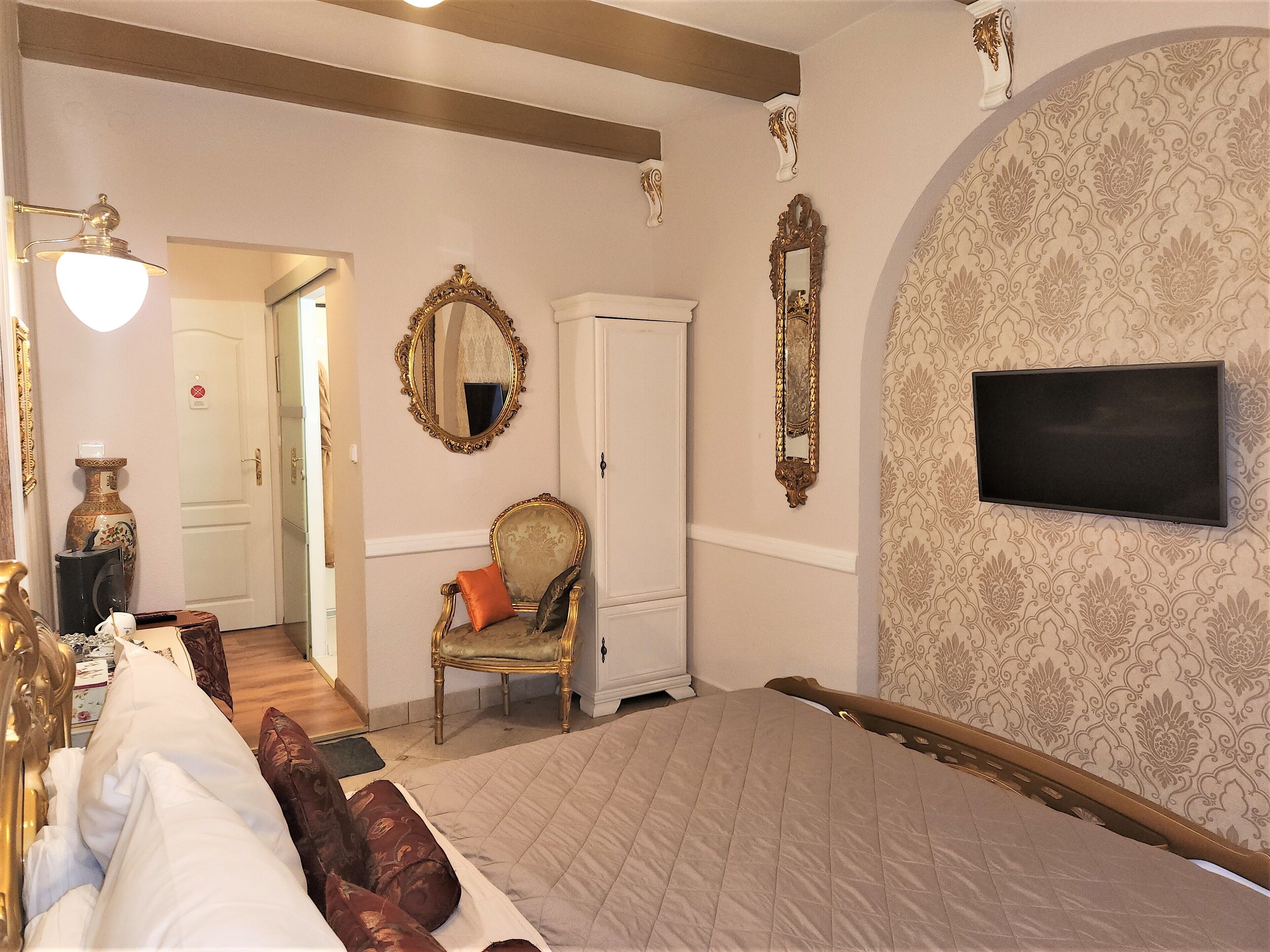 Une chambre avec un grand lit, un téléviseur fixé au mur, une chaise, une armoire et un miroir.