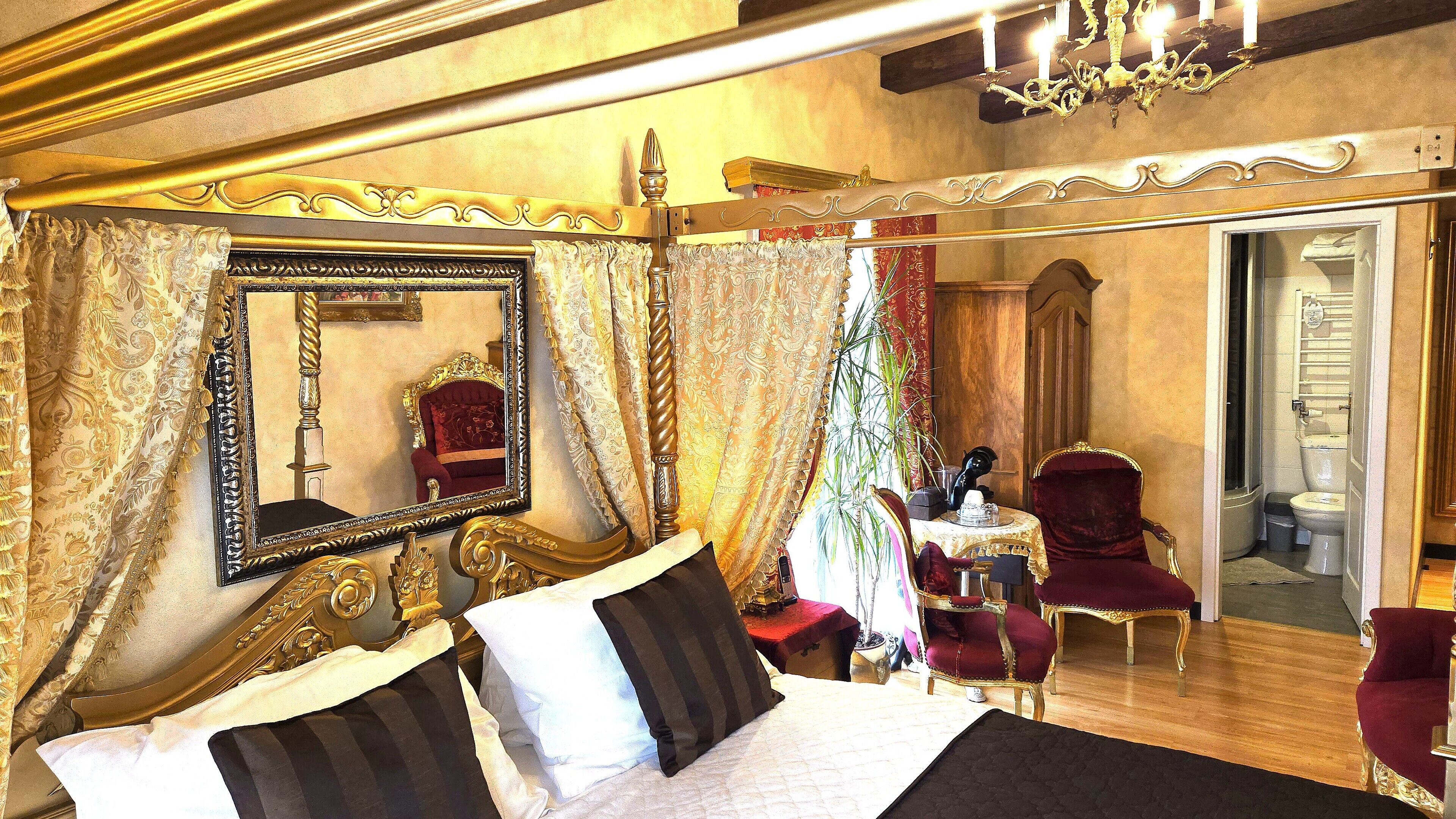 A luxurious bedroom with a large bed, ornate curtains, a mirror, and a chandelier.
