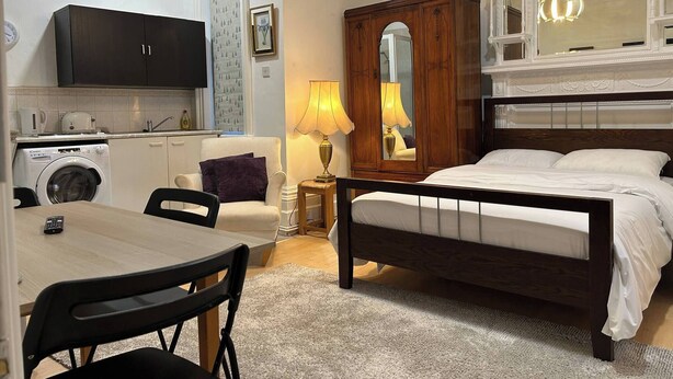 Une chambre à coucher avec un lit, une table de chevet, un miroir et une commode. Il y a une fenêtre donnant sur l’extérieur.