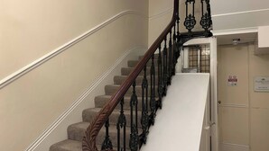 Un escalier orné de balustres noirs et doté d’une main courante en bois, menant à un palier où se trouve une porte sur laquelle est inscrit : « Il est interdit de fumer ou de vapoter. »
