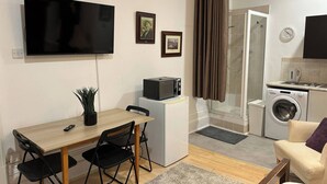 Un espace de vie compact comprenant un téléviseur, une petite table à manger avec des chaises, un lave-linge et une kitchenette.