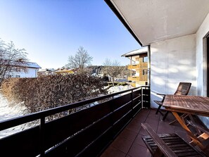 A balcony with a wooden table and chairs, overlooking a snowy landscape and buildings. - Staufenhirsch Apartment (Oberstaufen)