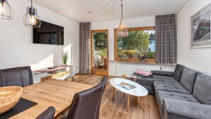 En moderne stue med et træspisebord, en grå sofa og et fjernsyn monteret på væggen.