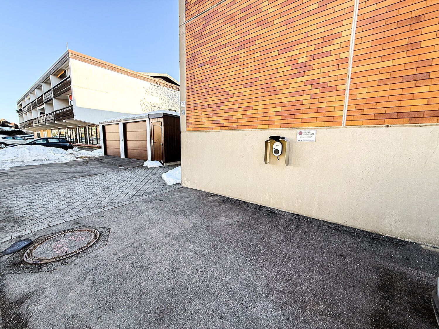 Ein Parkplatz mit einem Backsteinhaus, einer Garagentür und einer Überwachungskamera.