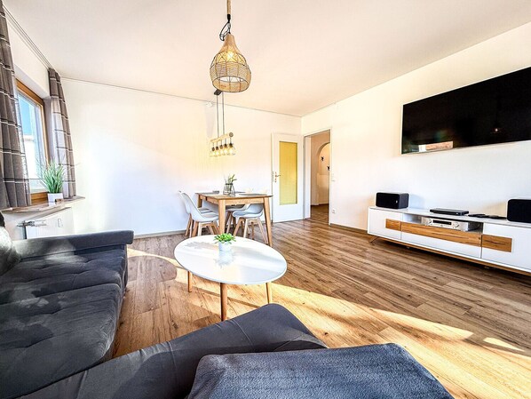 A modern living room with a sofa, a dining table, and a TV. - Staufenhirsch Apartment (Oberstaufen)