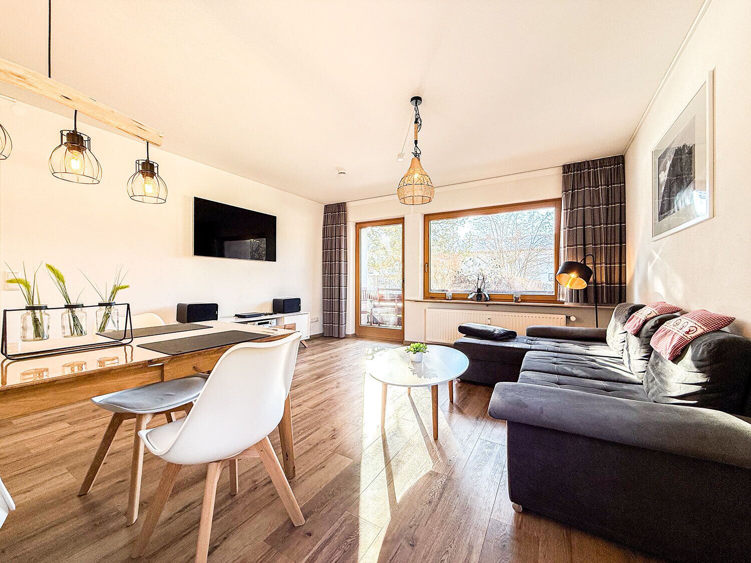 A modern living room with a sofa, a dining table with chairs, and a kitchen area with a counter and cabinets.