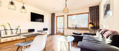 A modern living room with a sofa, a dining table with chairs, and a kitchen area with a counter and cabinets.