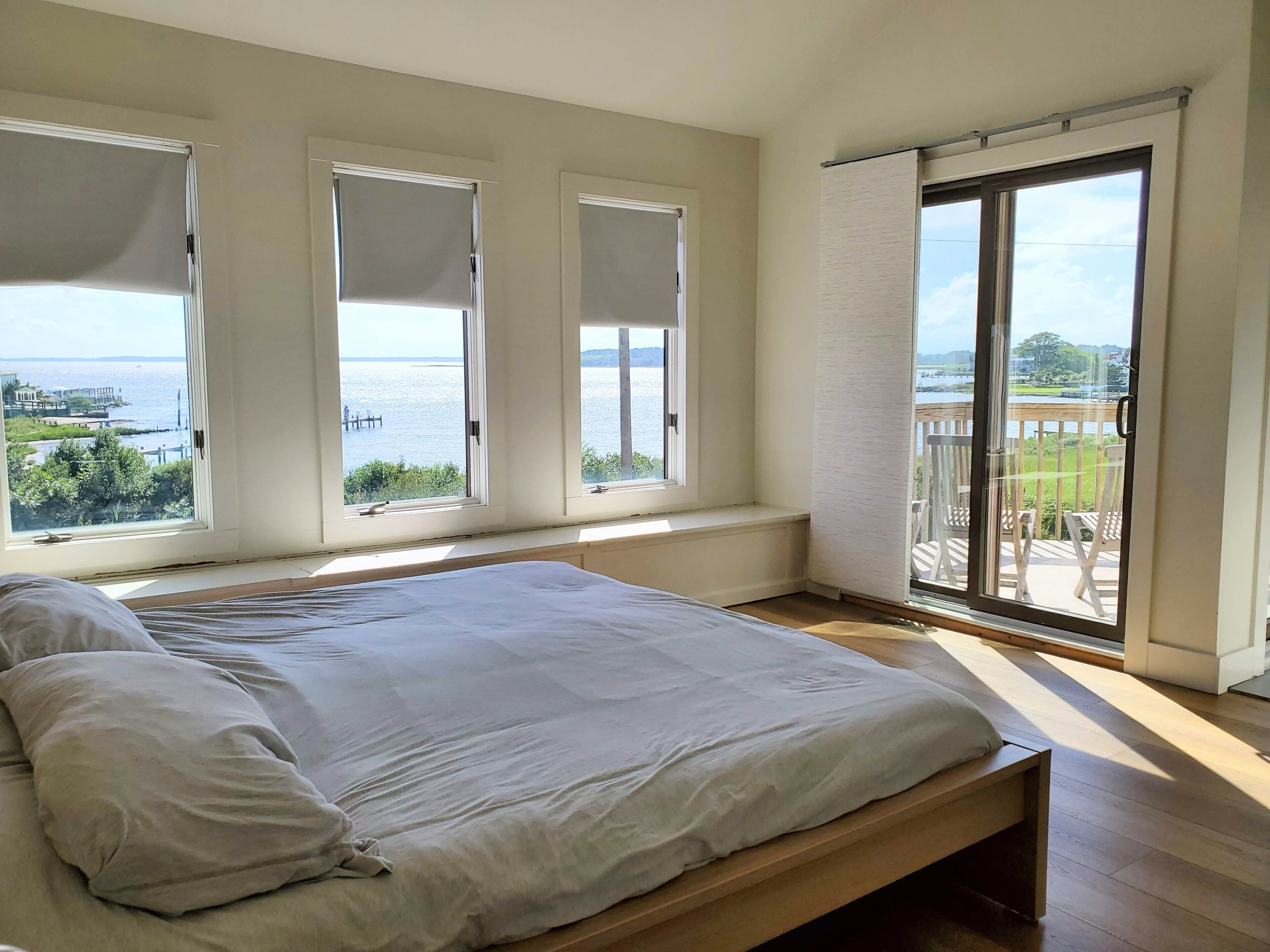 Ein Schlafzimmer mit einem großen Bett, drei Fenstern und einem Balkon mit Blick auf das Wasser.