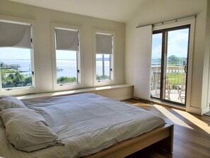 Ein Schlafzimmer mit einem großen Bett, drei Fenstern und einem Balkon mit Blick auf das Wasser.