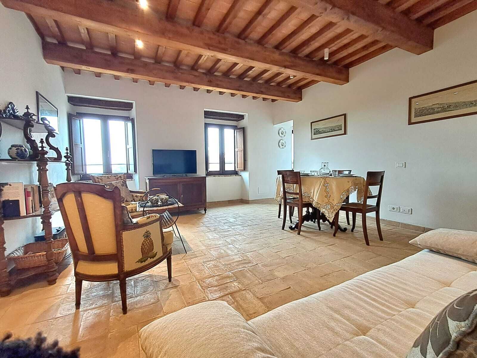 A spacious living room with a wooden ceiling, a television, a dining table with chairs, and a sofa.