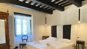 A bedroom with a large bed, a wooden wardrobe, a chair, a bedside table, and a window with curtains. - pieve san biagio (Macerata)