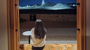 A person sitting at a table with a view of a night landscape through a wooden-framed window. - Soyeonjae hanokstay (Gyeongju)