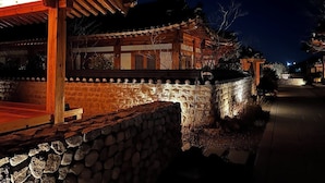 A traditional building with a stone wall and wooden structure, illuminated by warm lighting. - Soyeonjae hanokstay (Gyeongju)