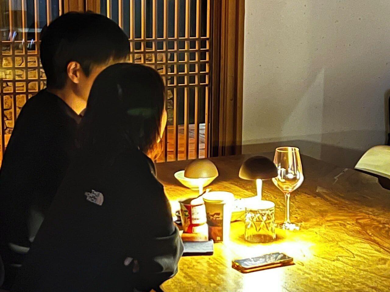 Una pareja sentada en una mesa con una vela, una copa de vino y una lámpara.