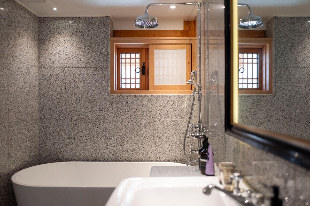 A modern bathroom with a freestanding bathtub, a shower with a handheld showerhead, and a window with wooden frames.