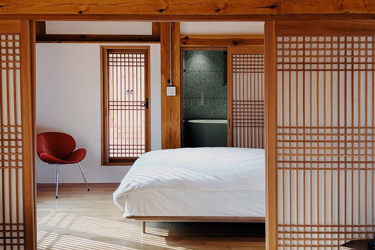 Une chambre de style japonais traditionnel, avec un plafond en bois, des portes coulissantes, un lit et une chaise rouge.