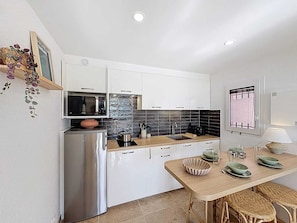 A compact kitchen with white cabinets, a stainless steel refrigerator, a microwave, and a sink. - Appartement 4 personnes, climatisé, Wifi, parking, piscine et vue mer ! (Cavalaire-sur-Mer)