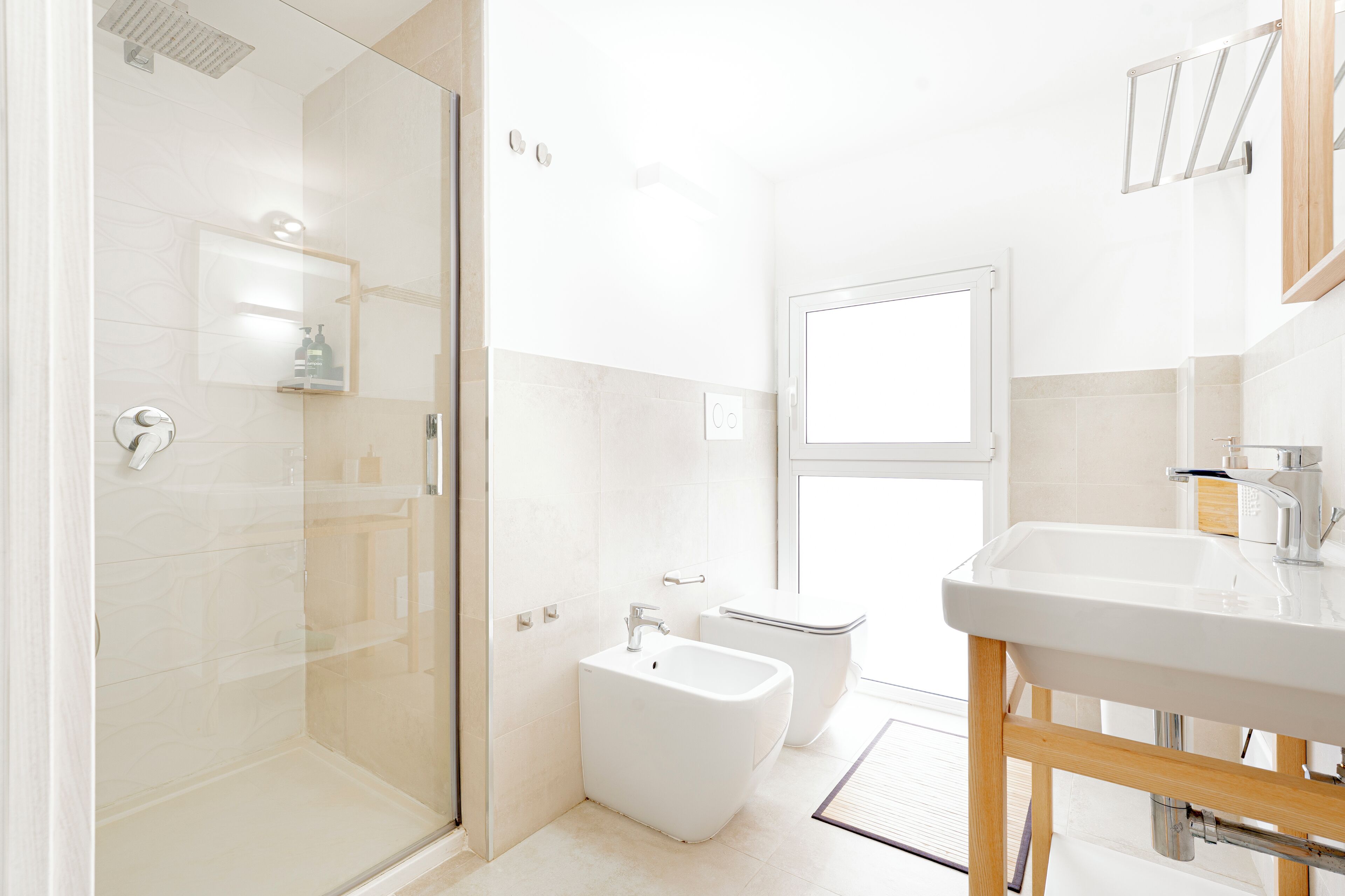 A modern bathroom with a glass-enclosed shower, a bidet, and a sink with a wooden frame.