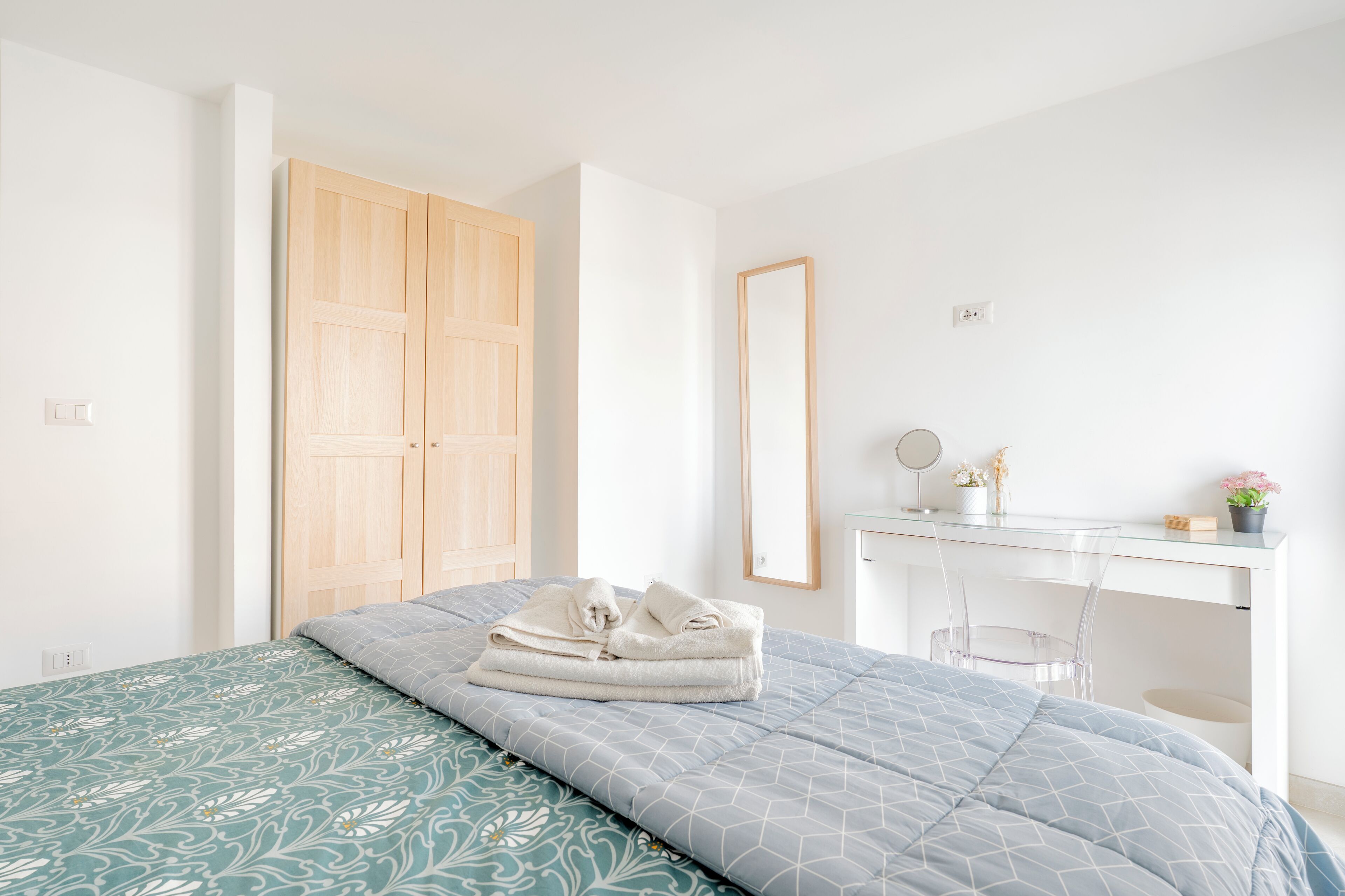 A bedroom with a bed, a desk, and a wardrobe.