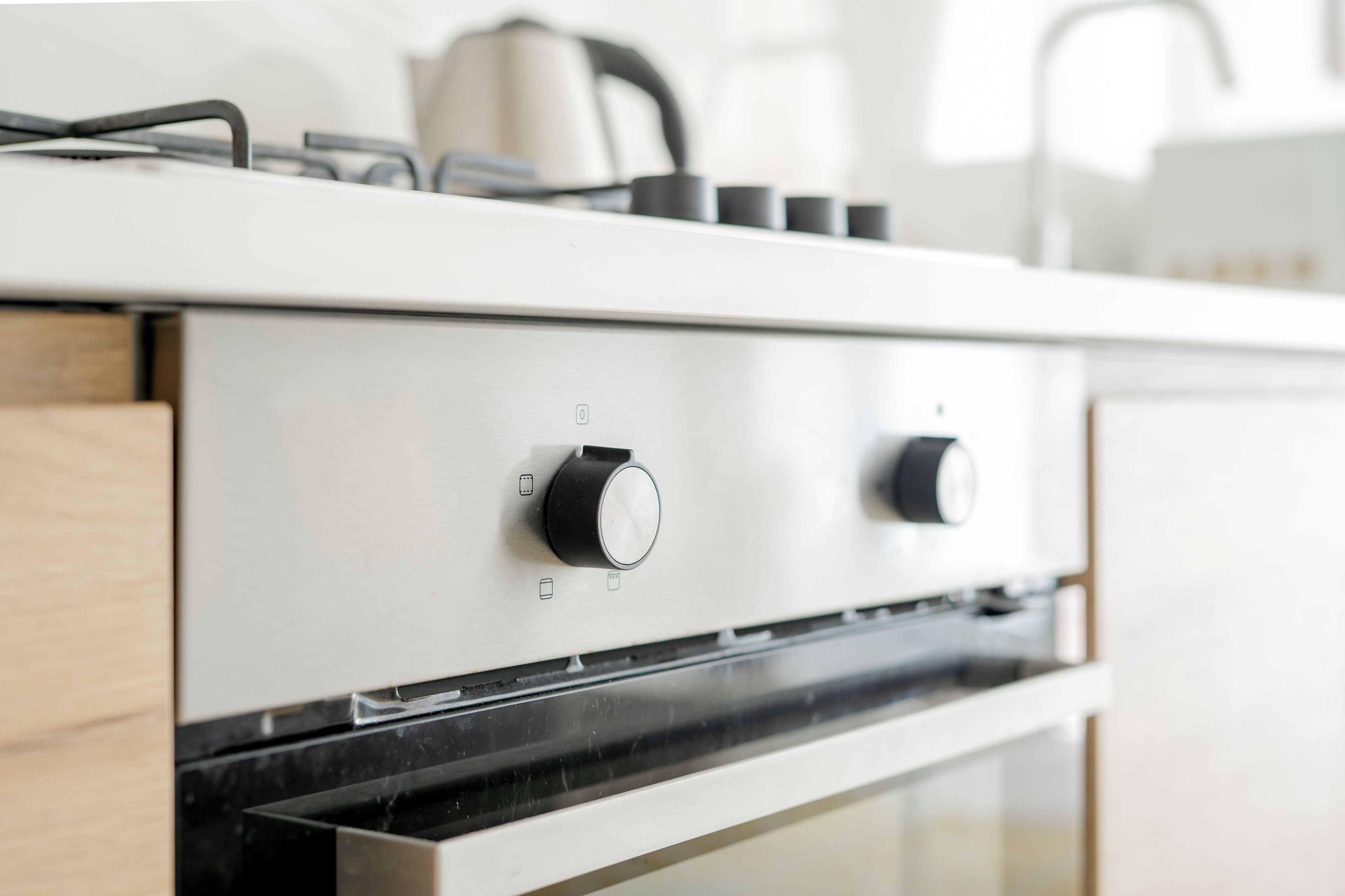 A modern kitchen with a stainless steel stove, two black knobs, and a kettle on the countertop.