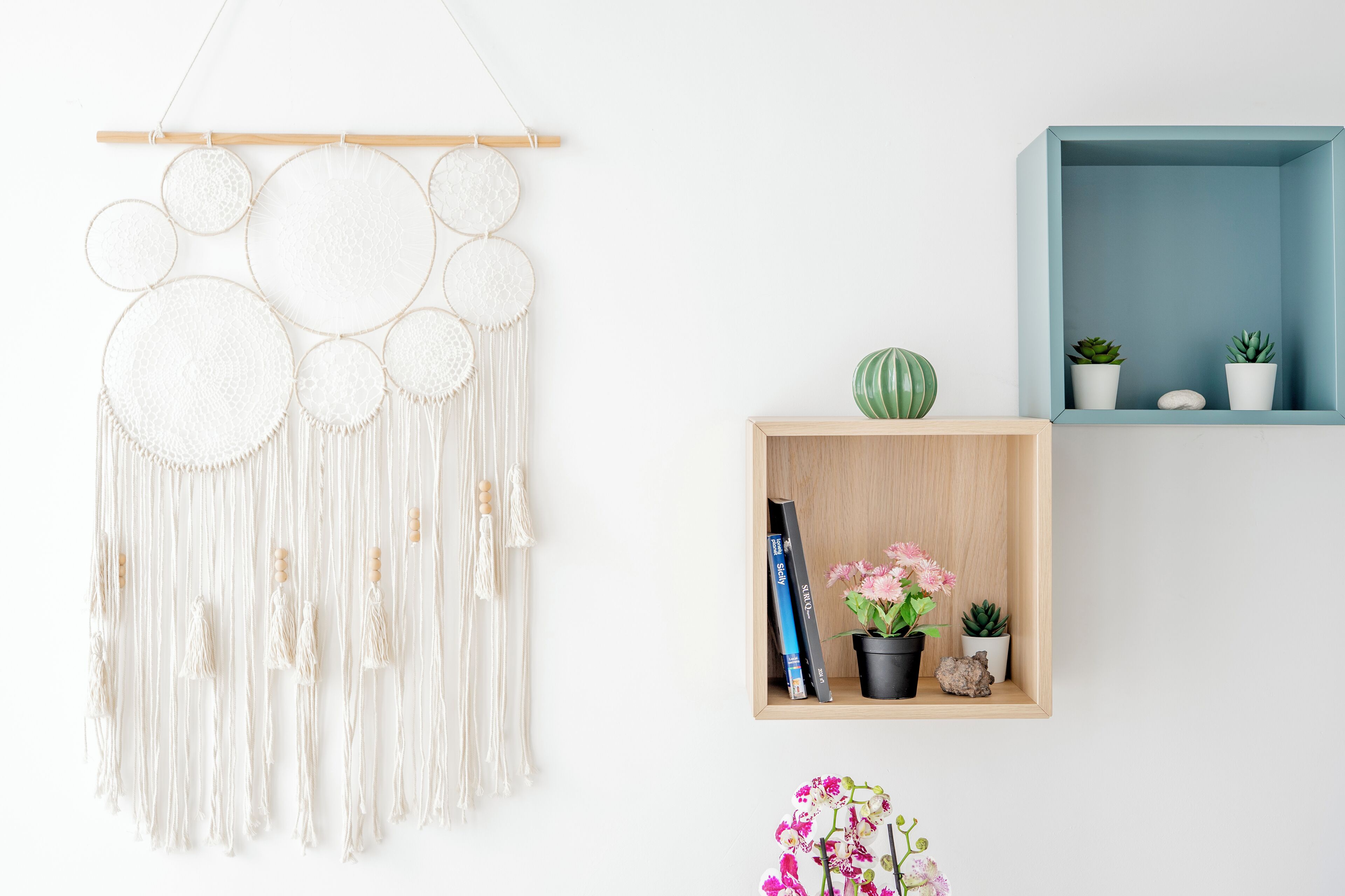 A macrame wall hanging, a wooden shelf with plants and books, and a blue storage box.