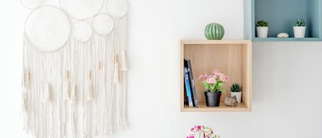 A macrame wall hanging, a wooden shelf with plants and books, and a blue storage box.