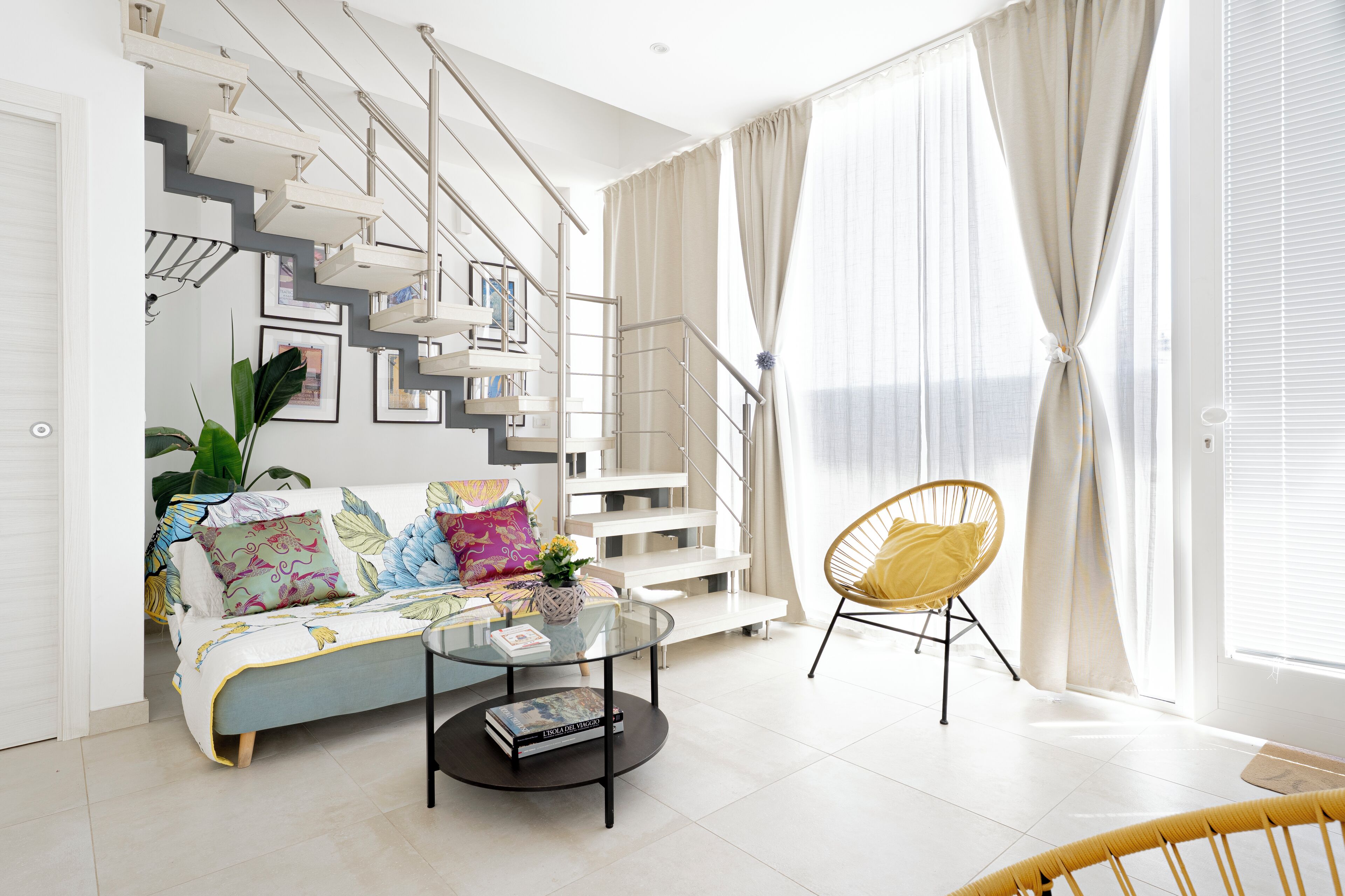 En moderne stue med trappe, sofa, sofabord og en gul stol.