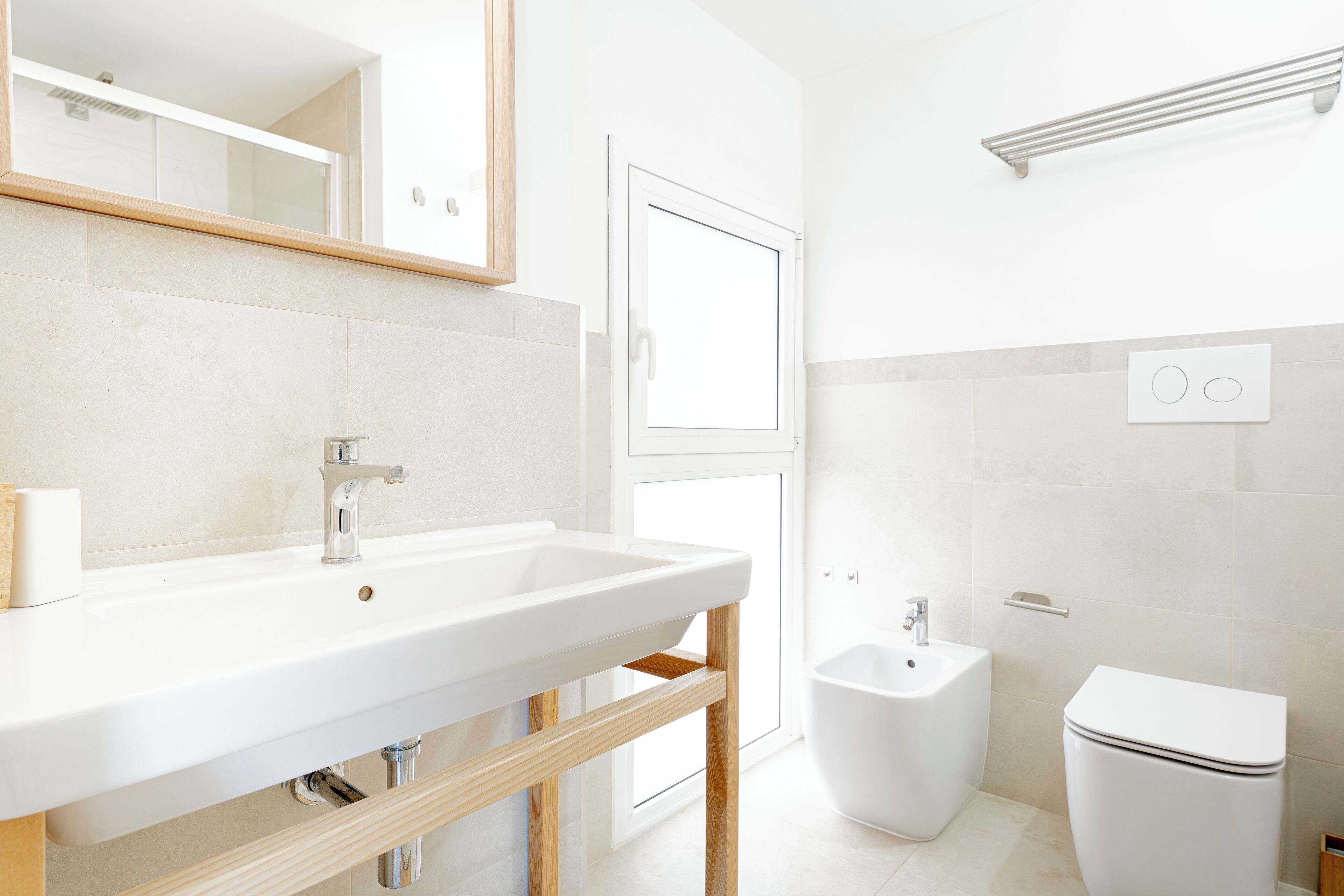 A modern bathroom with a white sink, mirror, and toilet.