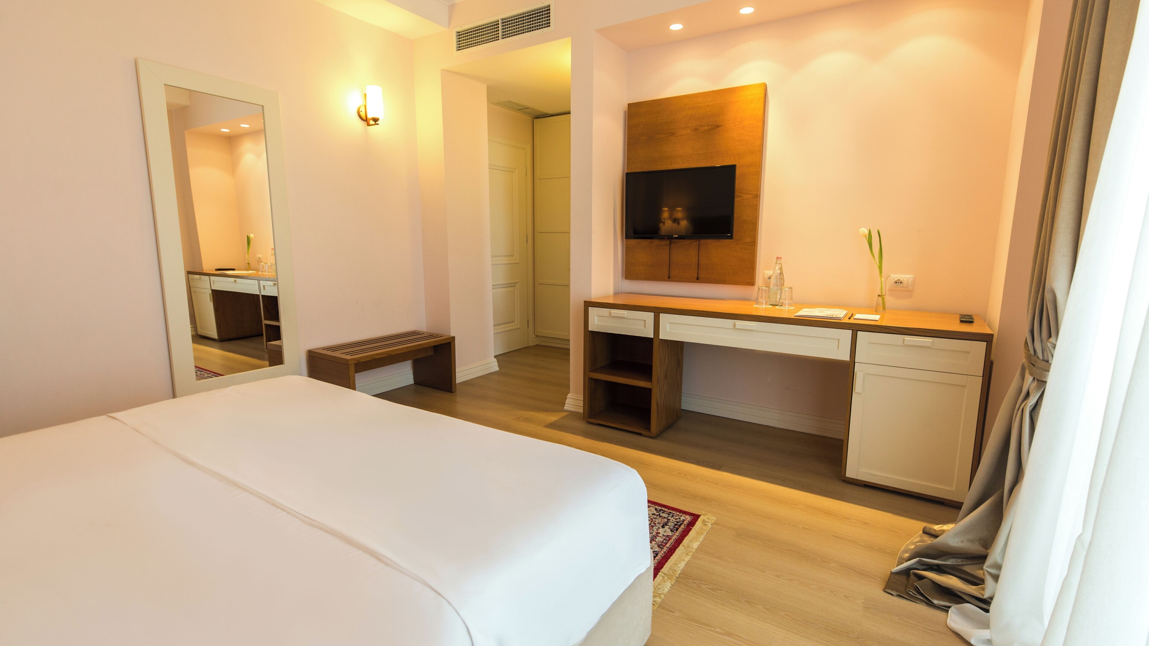 A hotel room with a bed, a desk, a television, and a bathroom visible through an open door.