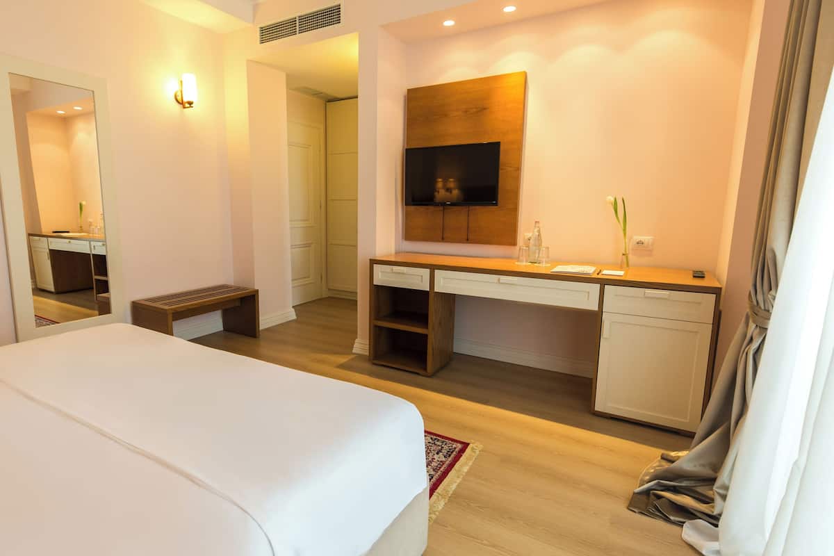 Quarto de hotel com cama, escrivaninha, televisão e banheiro visível através de uma porta aberta.